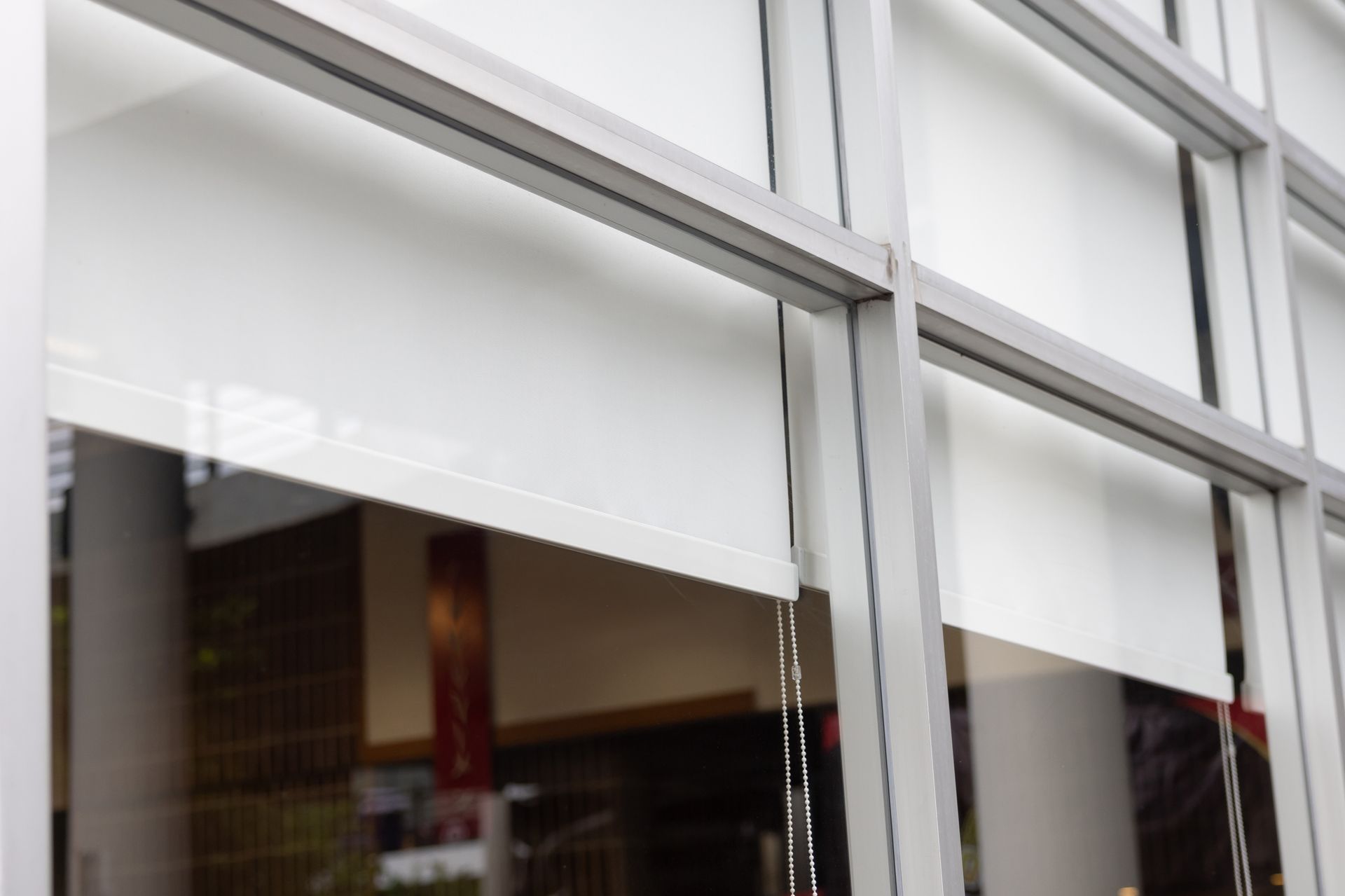 White window blinds inside a modern glass-fronted building