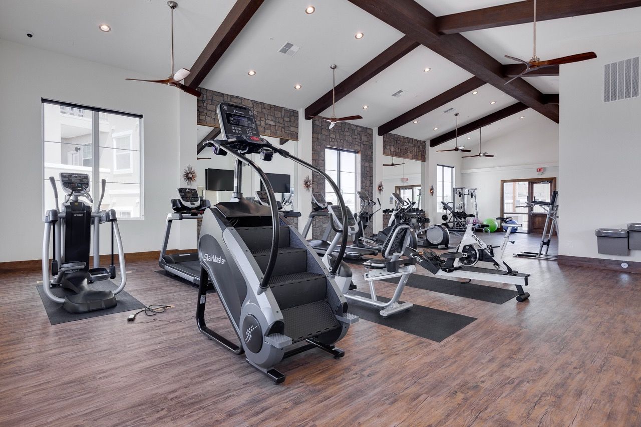 Modern community gym with treadmills, ellipticals, and bikes on wood flooring.