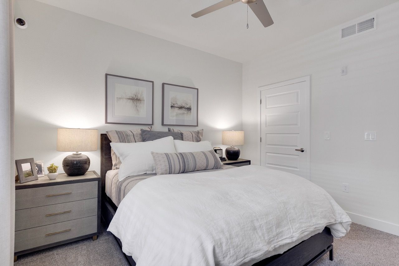Bedroom in a modern apartment with a queen bed, two nightstands, lamps, and framed artwork.