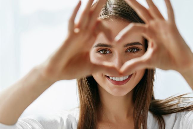 Smiling woman framing her face with her hands against a bright white background