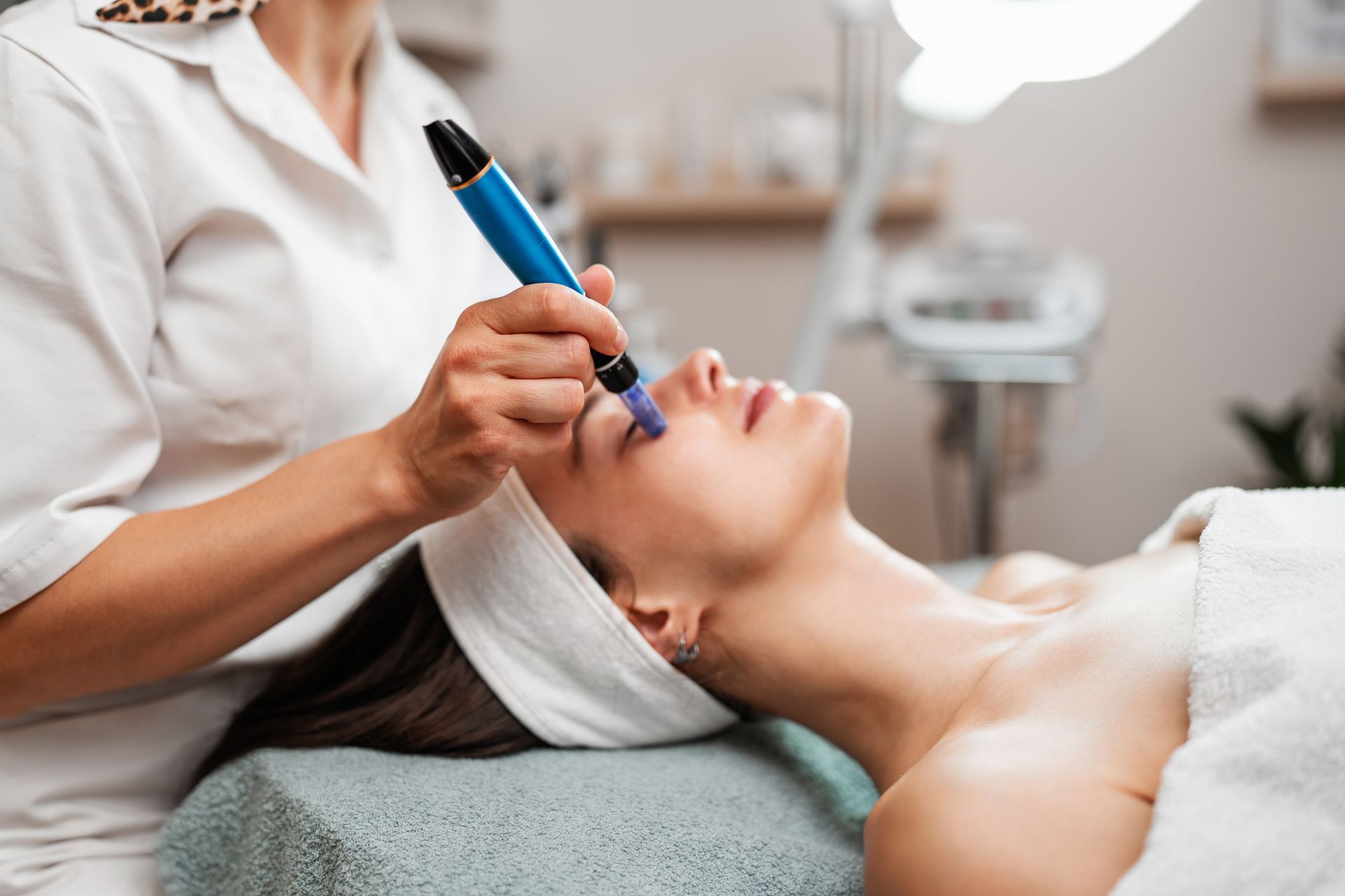 Cosmetologist applying a blue facial treatment tool to a client in a spa treatment room Cosmetologist applying a blue facial treatment tool to a client in a spa treatment room