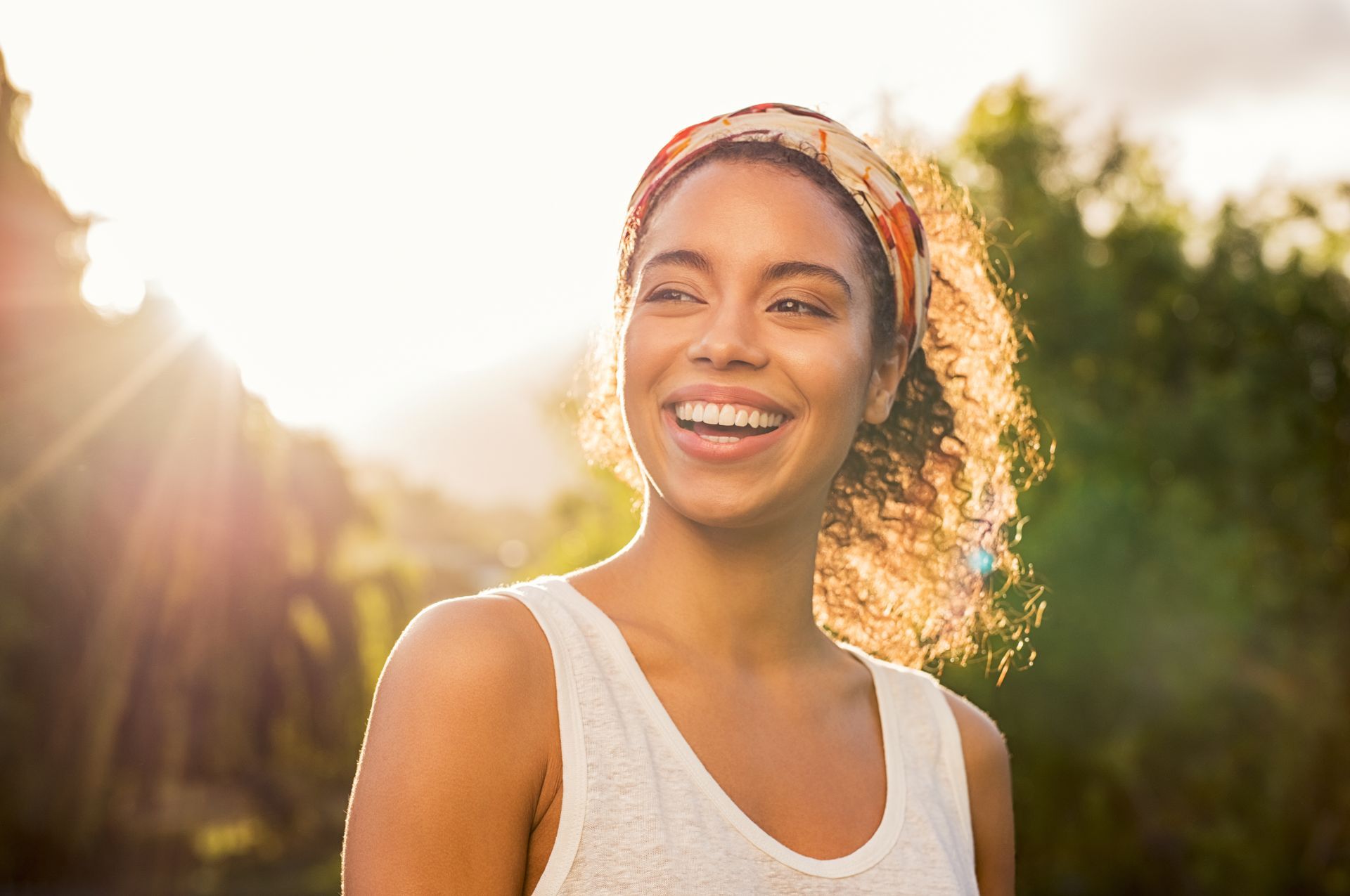 Smiling person in a white tank top outdoors at sunset, backlit by warm golden sunlight. Smiling person in a white tank top outdoors at sunset, backlit by warm golden sunlight.