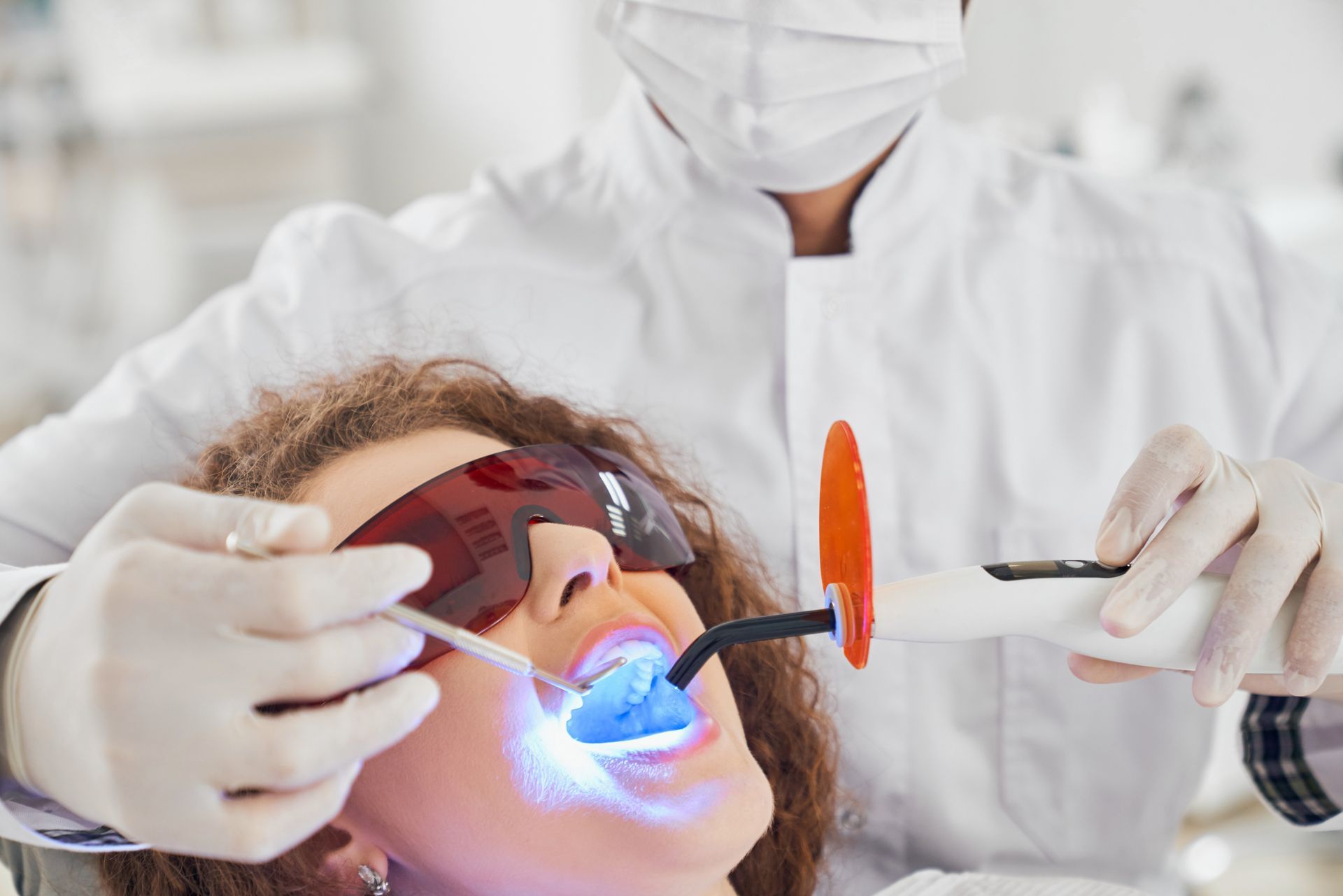 Dentist using tools on patient with glowing blue light during dental treatment Dentist using tools on patient with glowing blue light during dental treatment