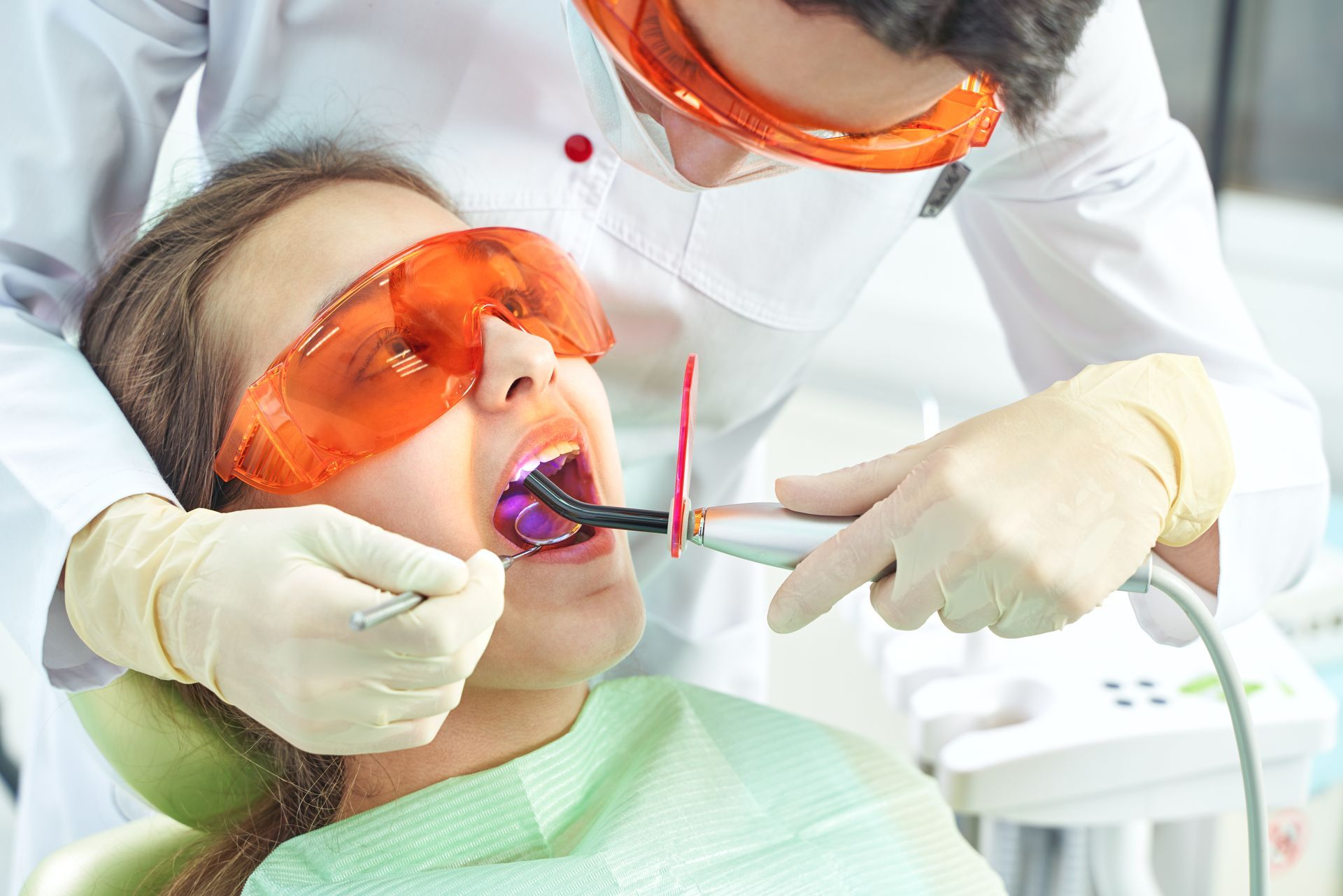 Dentist treating a patient wearing orange protective glasses during a dental procedure Dentist treating a patient wearing orange protective glasses during a dental procedure