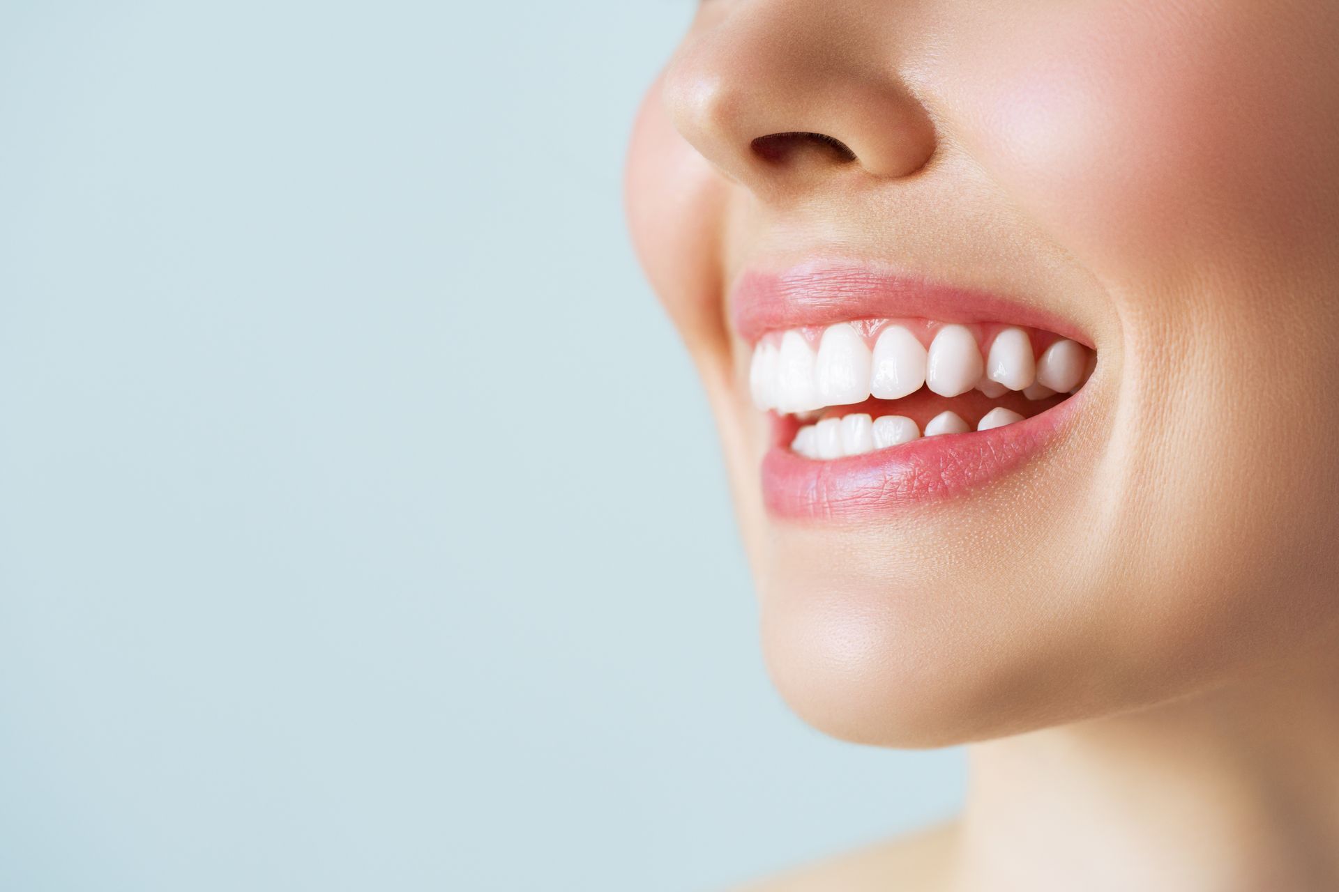 Close-up of a smiling mouth and nose with white teeth against a light blue background
