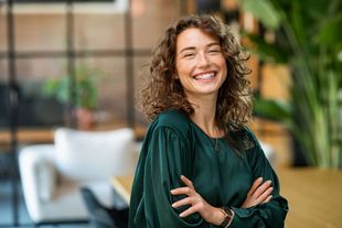 Smiling woman in a green blouse with arms crossed in a modern office setting Smiling woman in a green blouse with arms crossed in a modern office setting