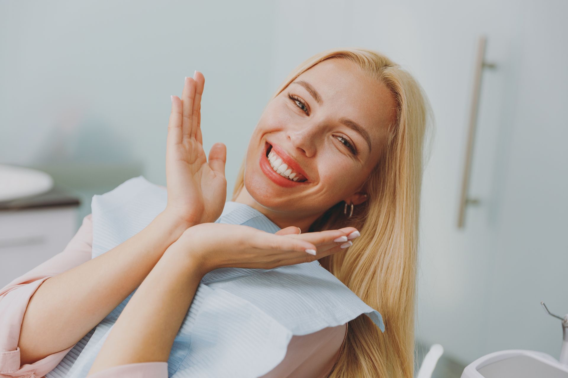 Smiling blonde woman posing in a bright room, resting her chin on her hands