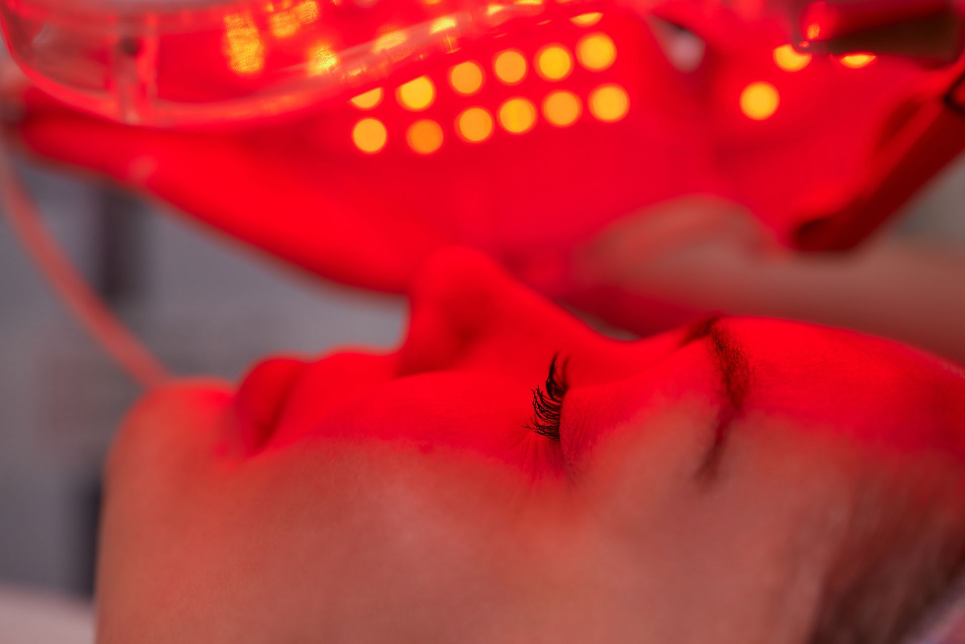 Close-up of a face under red light therapy with a glowing LED device above it Close-up of a face under red light therapy with a glowing LED device above it