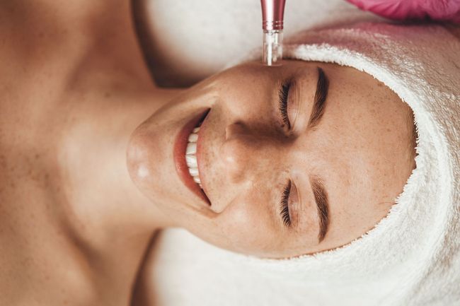 Woman receiving facial treatment with a serum dropper while wrapped in a white towel