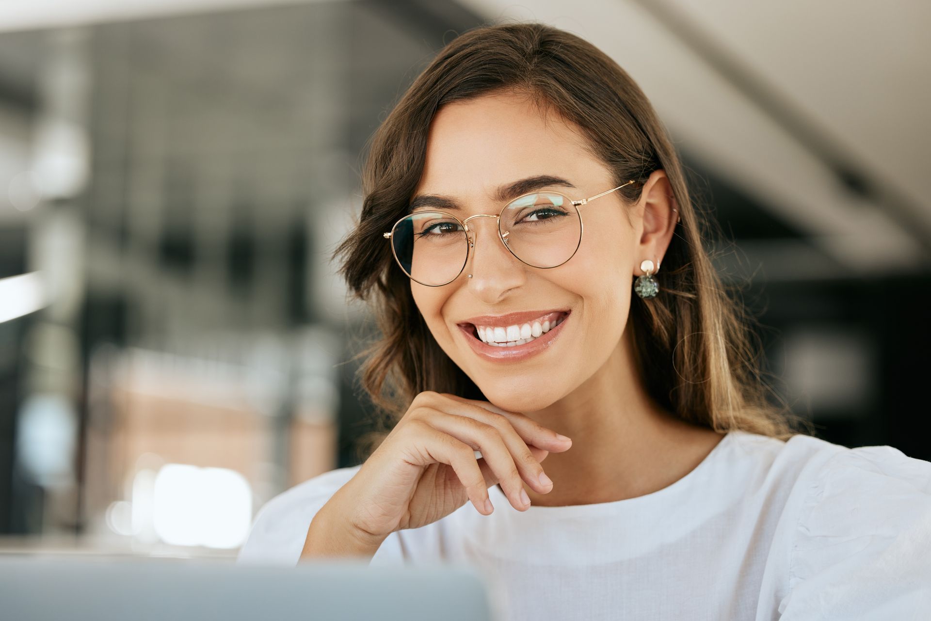 Smiling person with glasses resting chin on hand in a bright office setting