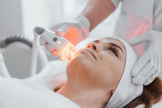Facial treatment with glowing device applied to a woman's cheek in a spa setting