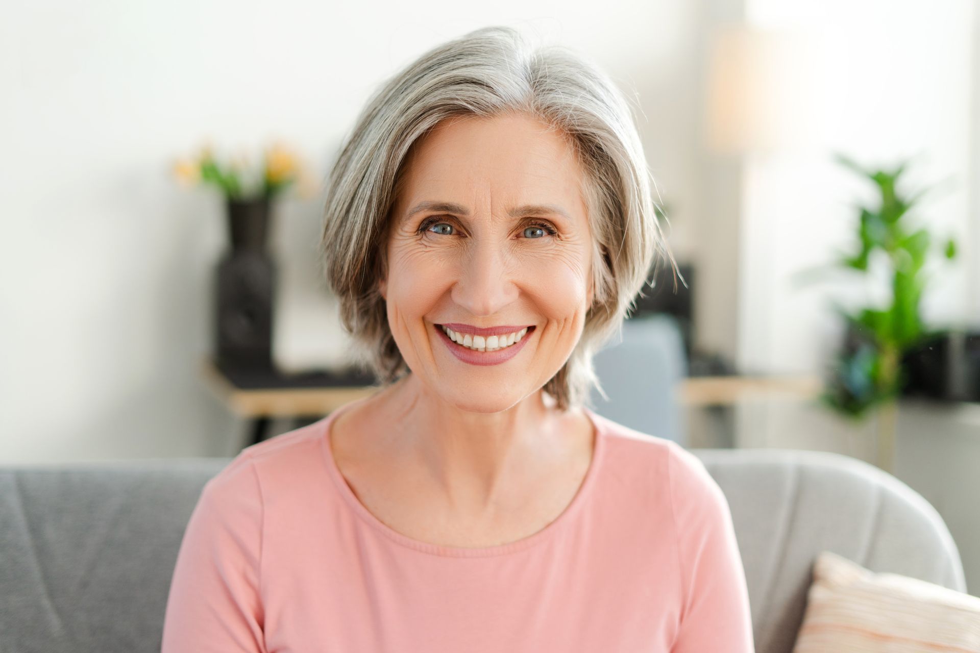 Smiling woman in a pink top seated on a gray sofa in a bright living room