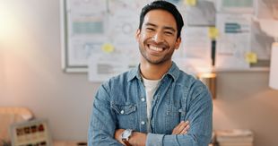 Smiling man in a denim shirt standing with arms crossed in a bright office setting Smiling man in a denim shirt standing with arms crossed in a bright office setting