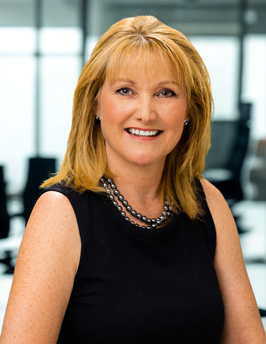 Smiling woman in a black sleeveless top and necklace standing in an office setting