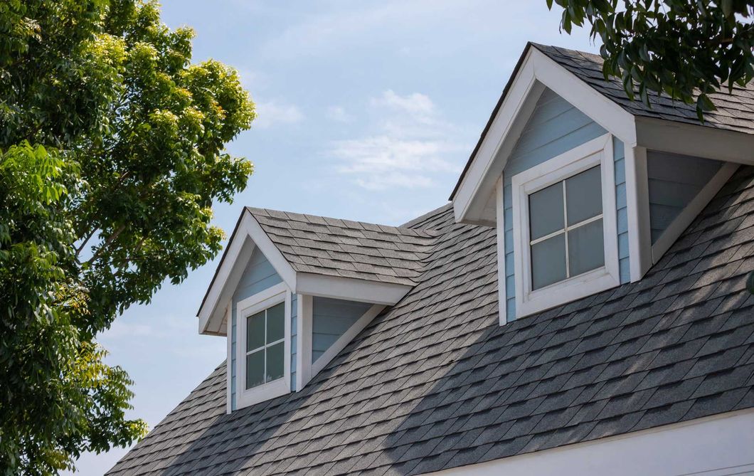 Light blue dormers with white trim on a gray shingled roof under a partly cloudy sky.