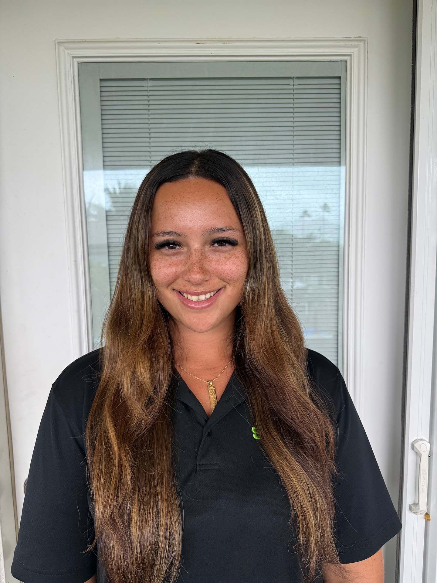 Smiling person standing in front of a door, wearing a black shirt