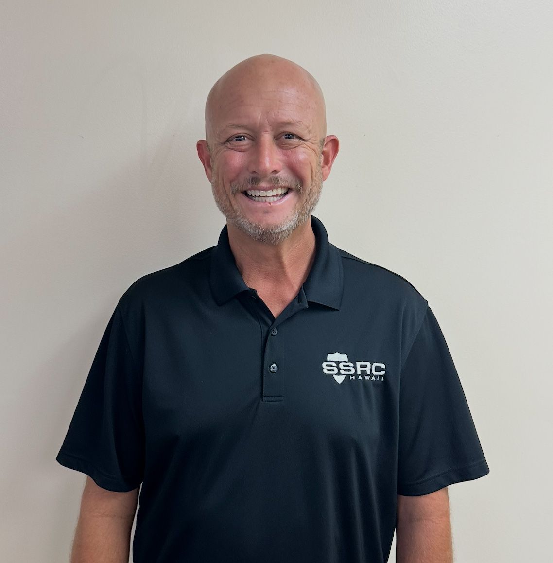 Smiling man in a navy polo shirt standing against a plain wall
