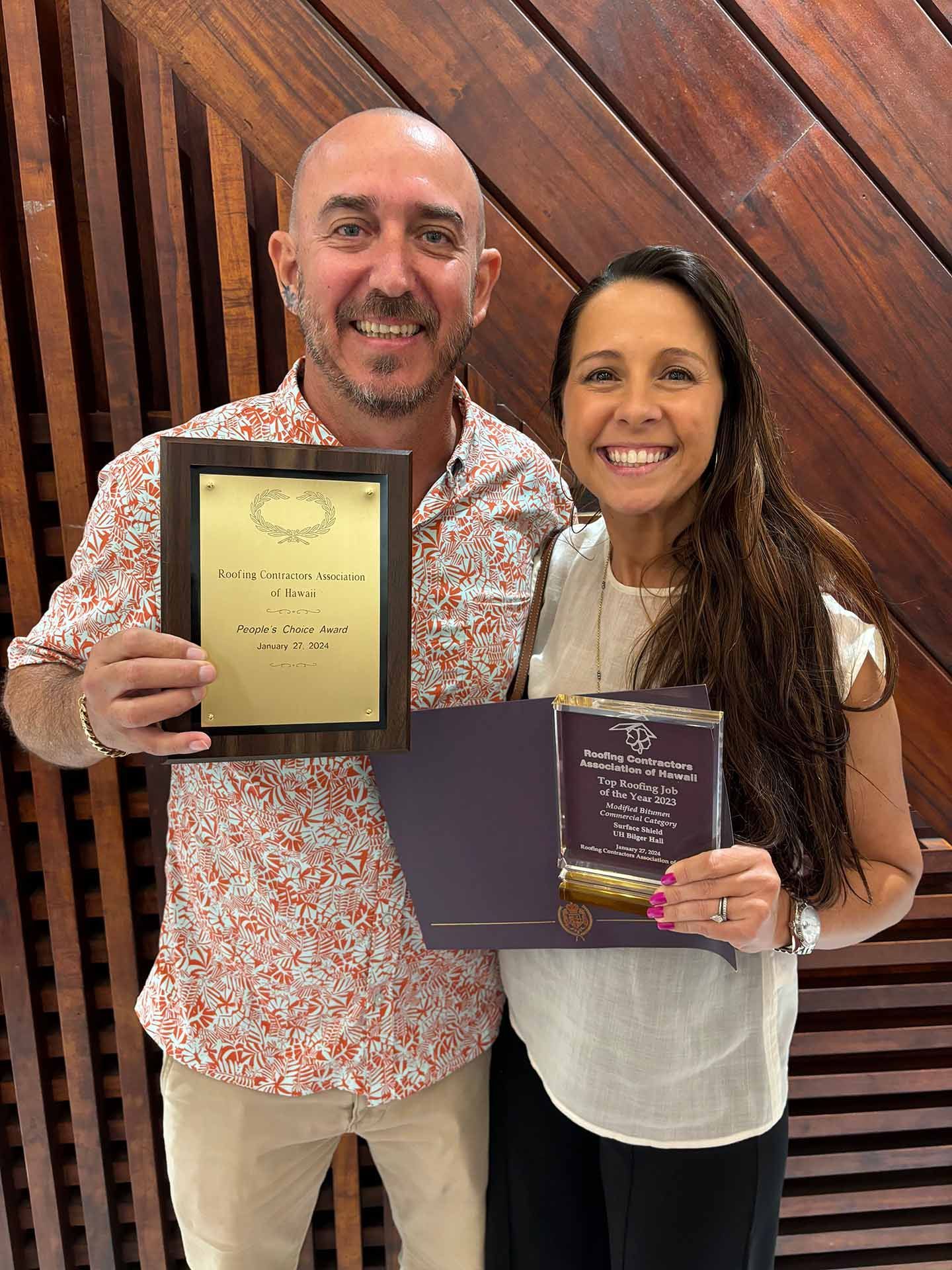 Two people smiling and holding certificates in front of a wooden wall