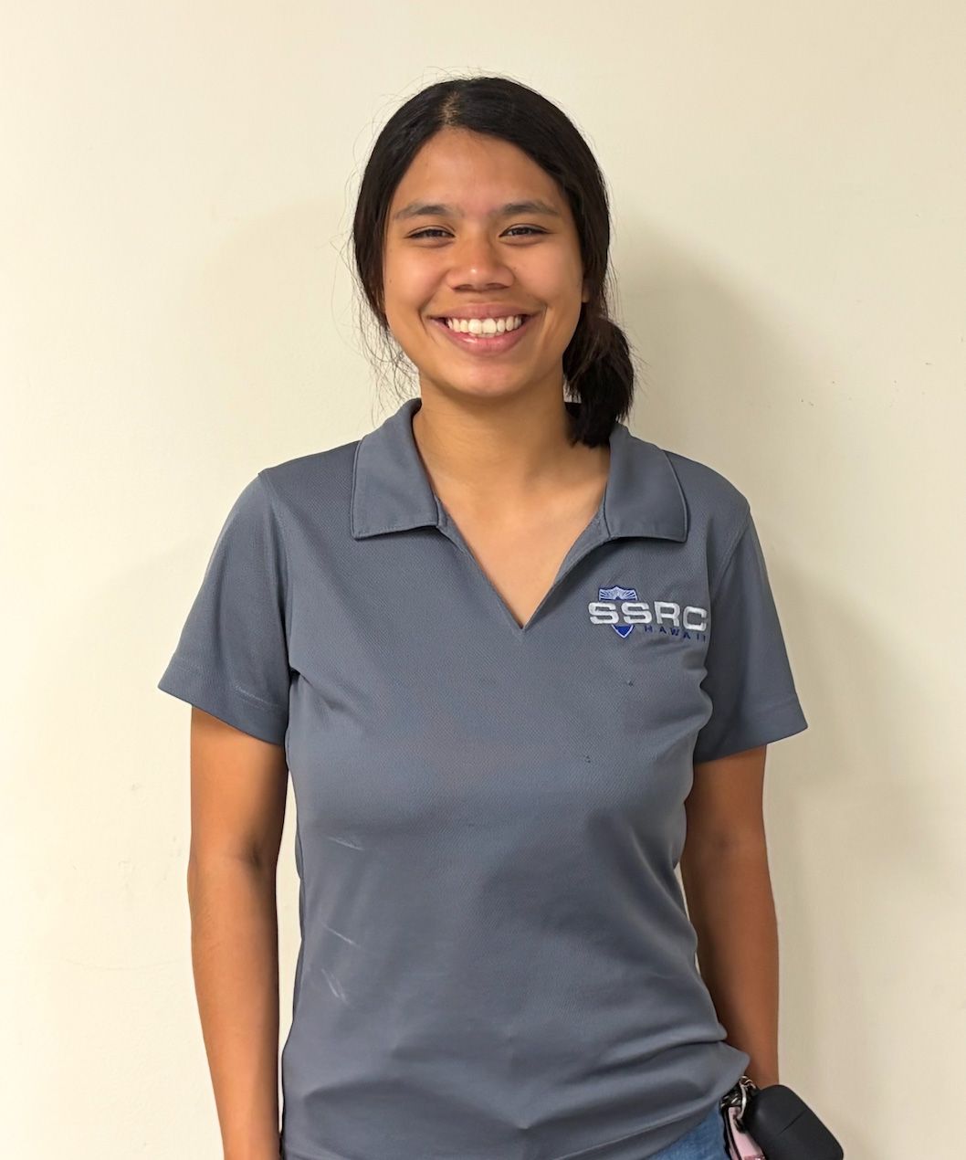 Smiling person in a gray polo shirt standing against a plain light wall