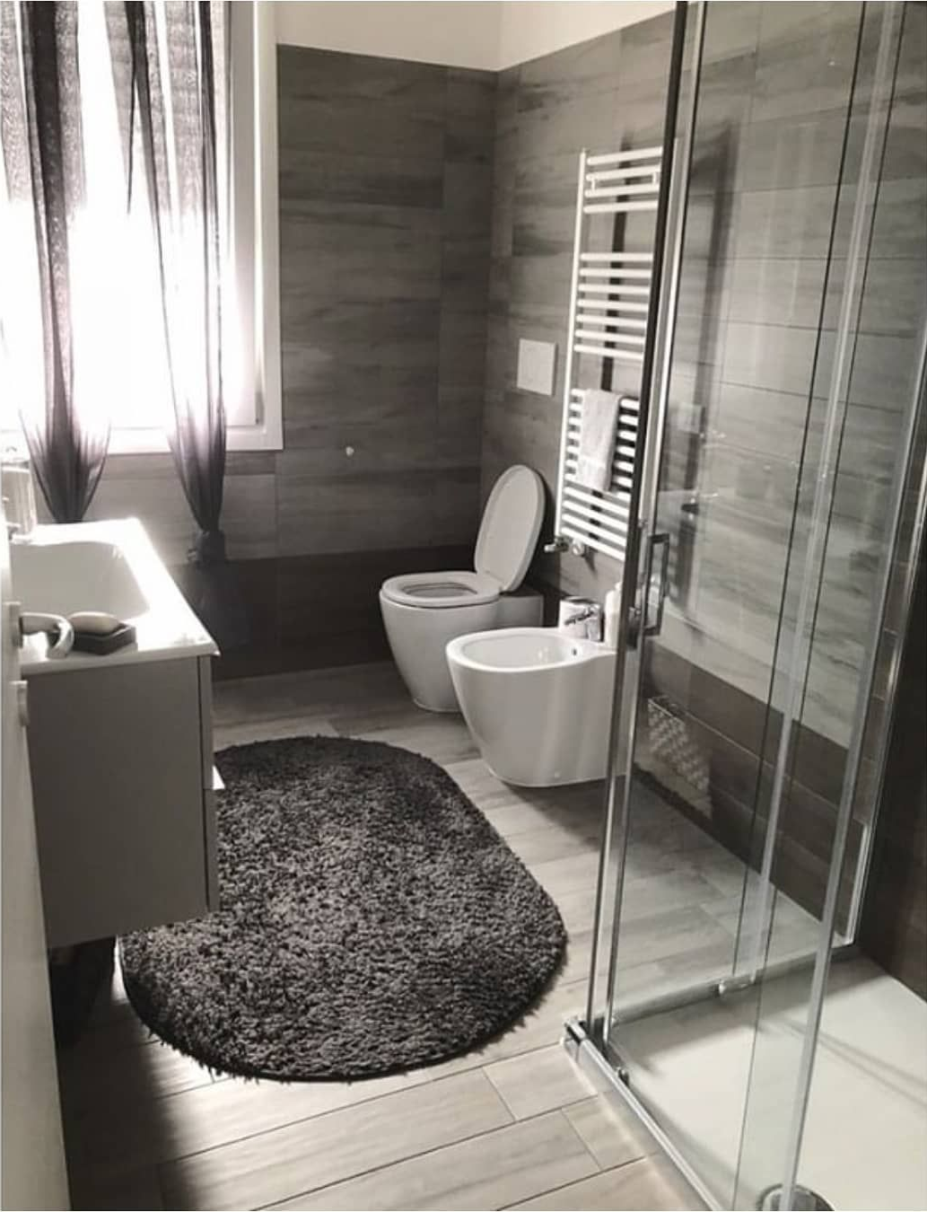 Bagno moderno con WC, bidet, lavandino, doccia e scaldasalviette. Pareti grigio scuro e tappeto.