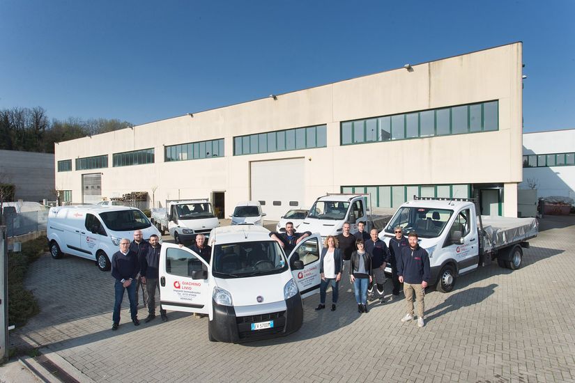 Un gruppo di persone staziona davanti a un edificio con i veicoli aziendali.