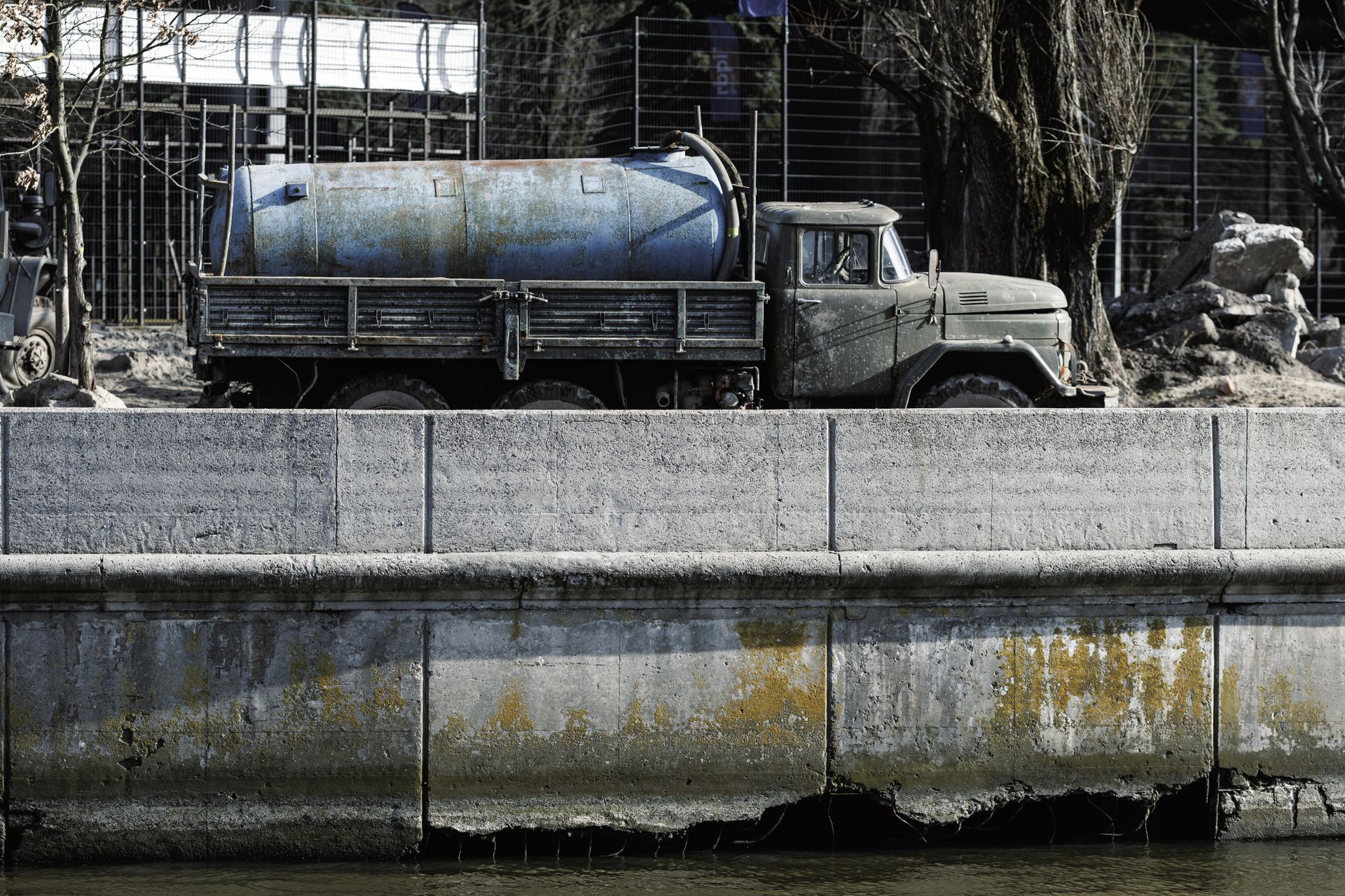 Black utility tank with blue pipes beside a building in a sandy outdoor area