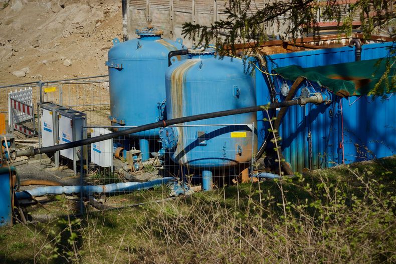 Green septic tank lids with an open circular access hole and black corrugated pipe in a dirt yard