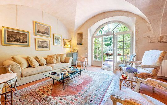 Bright sunlit living room with cream sofa, patterned rug, glass table, and arched French doors to a garden