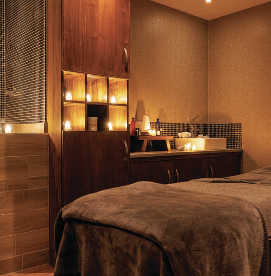Warm spa treatment room with a massage table, candles, and soft amber lighting