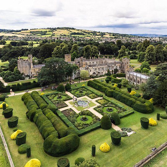 Formal garden with geometric hedges and a historic manor set in a green countryside landscape.