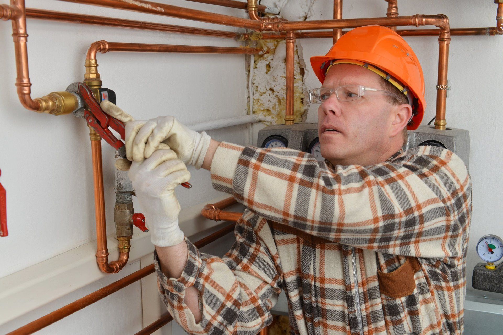 Ask about the warranty available for our new boilers A person in a hard hat and plaid shirt uses a wrench to tighten a valve on a copper pipe system.