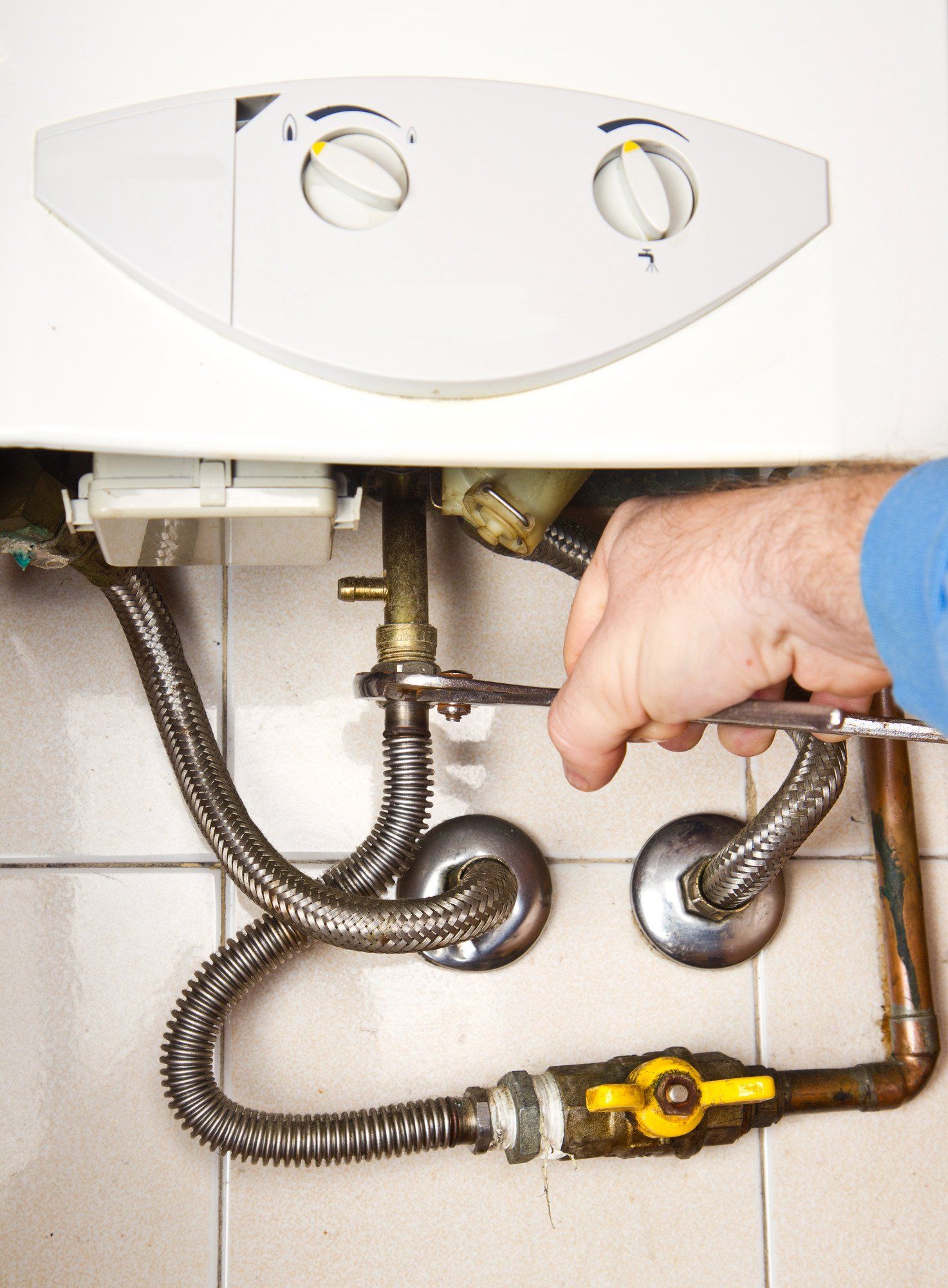 Ask about the warranty available for our new boilers A technician uses locking pliers to tighten a copper pipe fitting on a wall-mounted boiler unit.