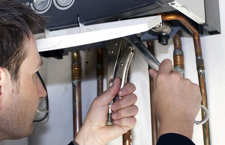 Ask about the warranty available for our new boilers A technician uses locking pliers to tighten a copper pipe fitting on a wall-mounted boiler unit.