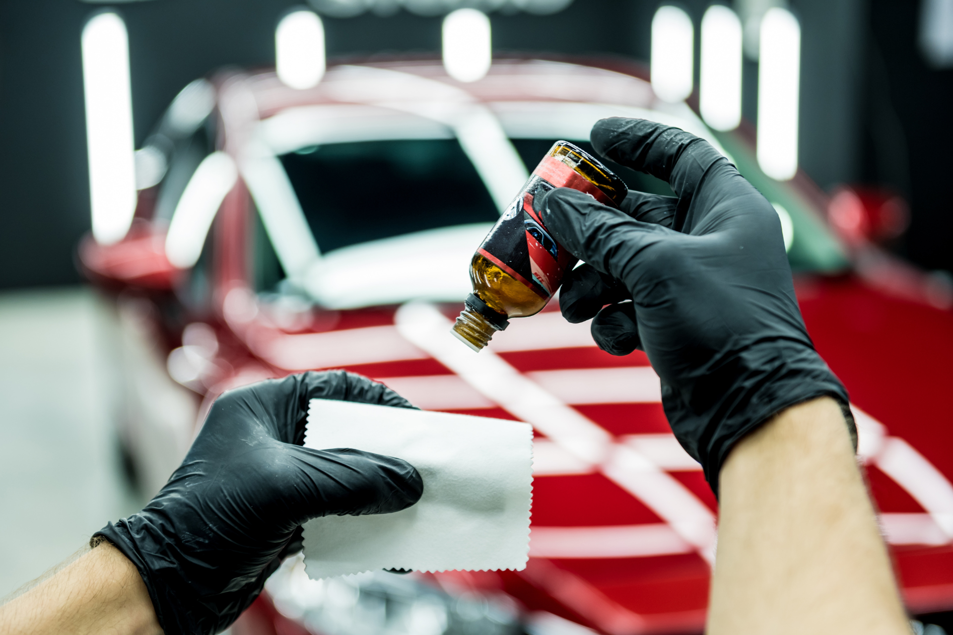 A person wearing black gloves is applying a coating to a red car.