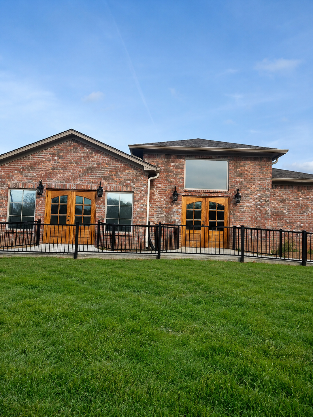Brick duplex with wood doors and black railing, viewed from a grassy yard under a blue sky