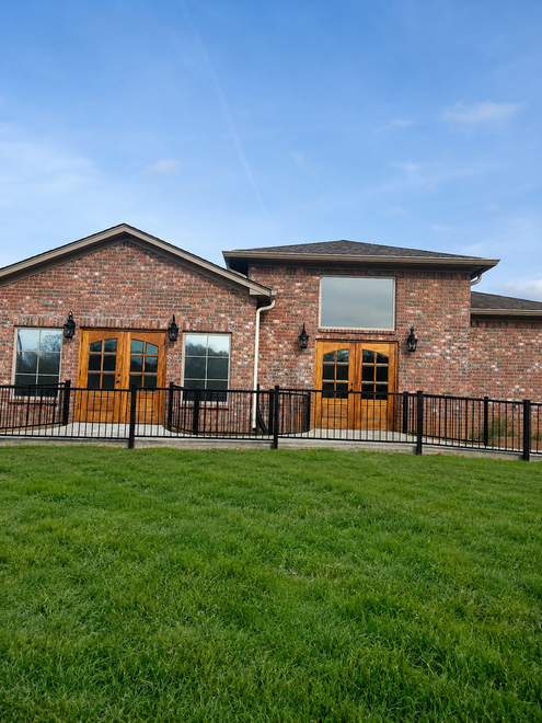 Brick building with wooden double doors, black railing, and green lawn under a blue sky