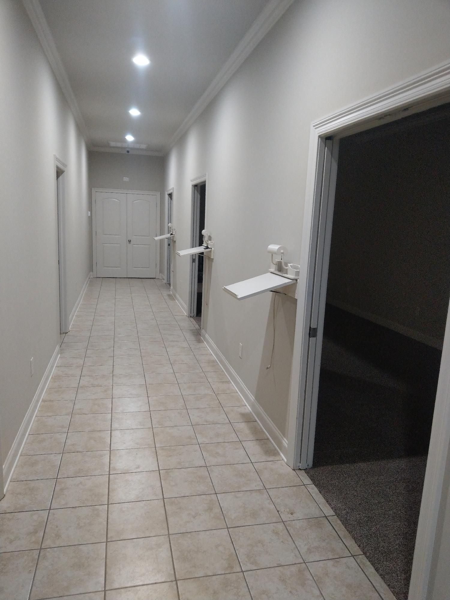 Narrow tiled hallway with white walls, ceiling lights, and open doorways on the right.