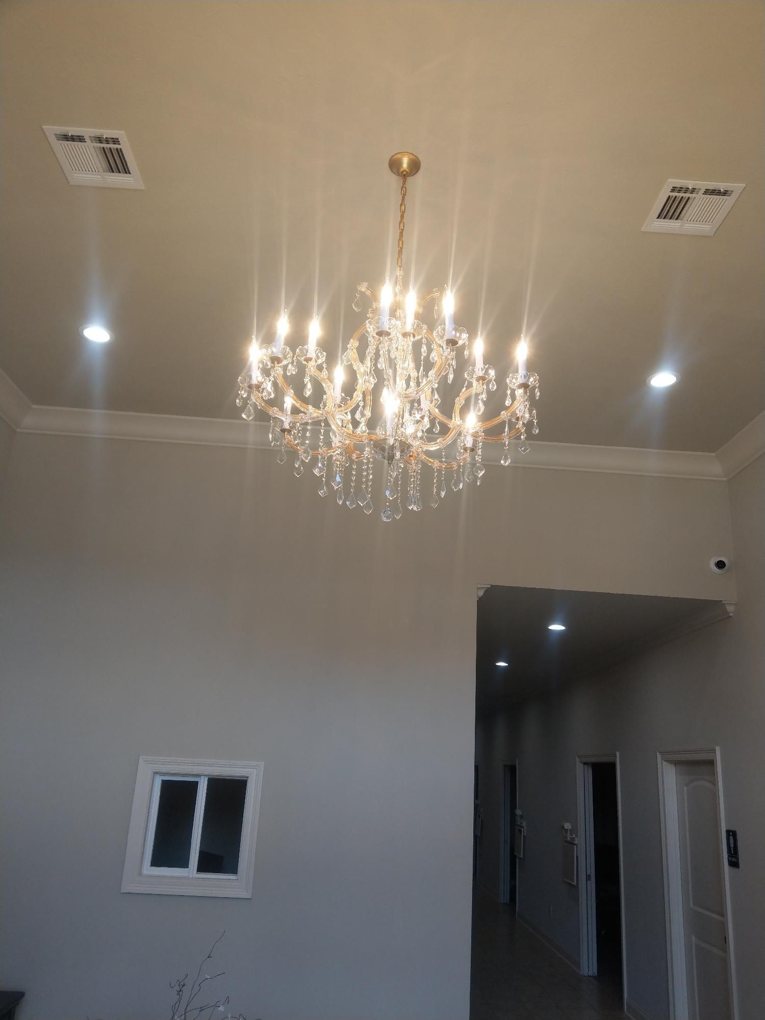 Crystal chandelier hanging from a white ceiling in a modern room with recessed lights and a doorway.