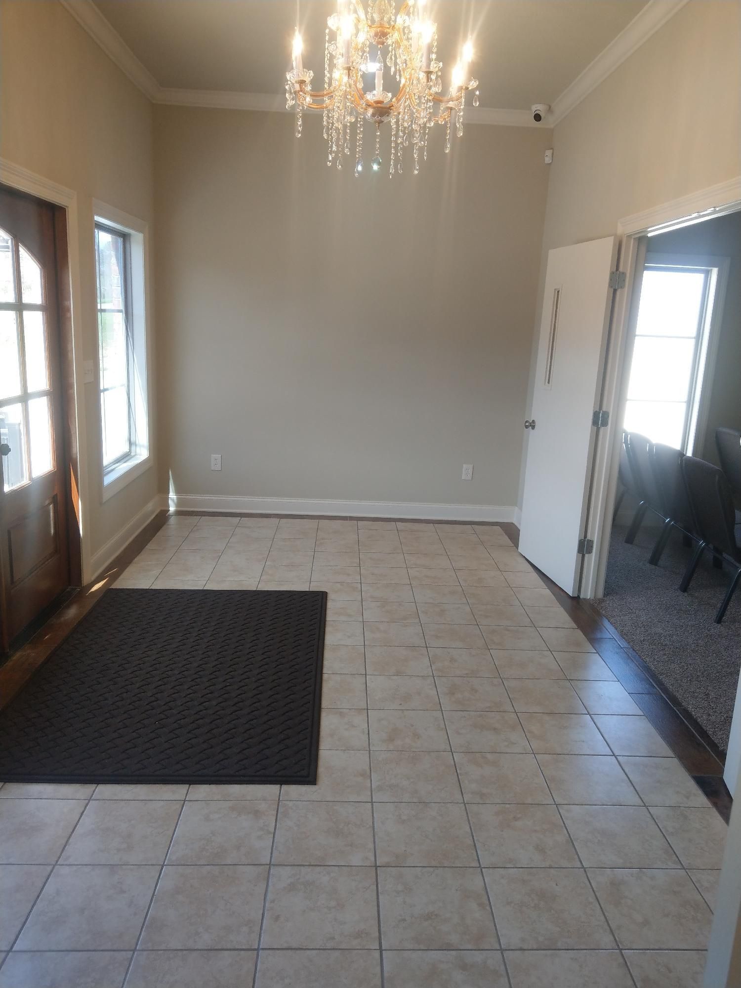 Empty tiled foyer with chandelier, light walls, and doors/windows on both sides.