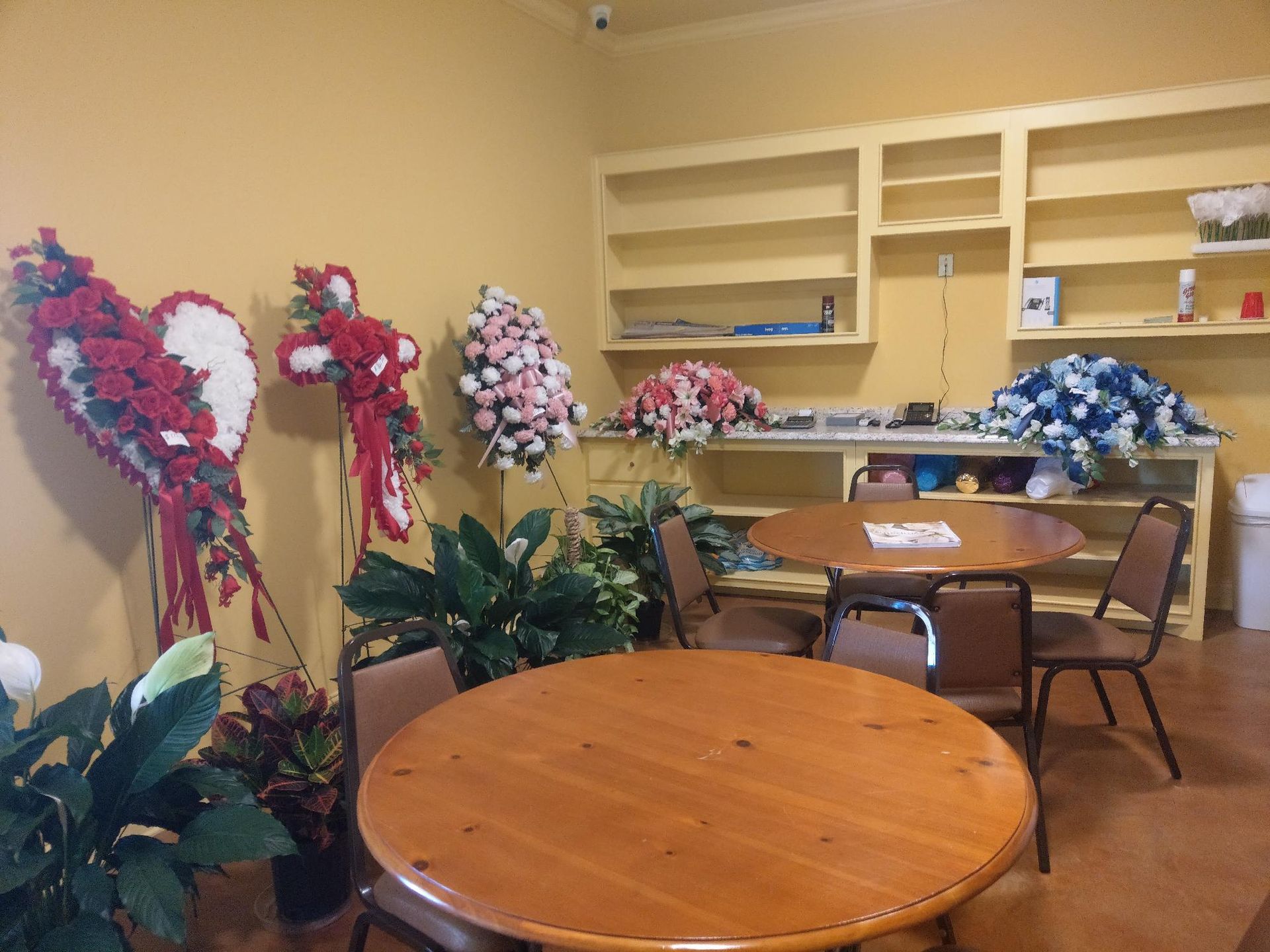 Flower-filled room with round tables, chairs, and shelves, decorated with pink, white, and blue arrangements