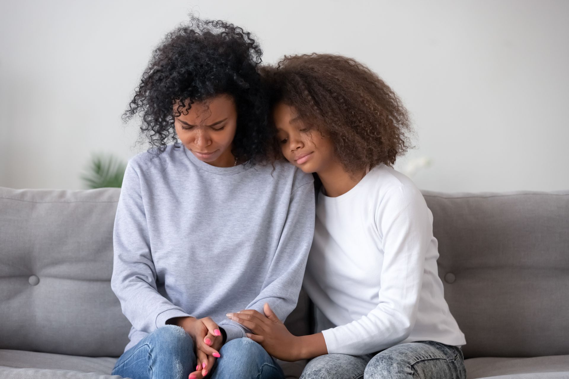 Two people sitting close on a gray couch, looking down at a phone together.