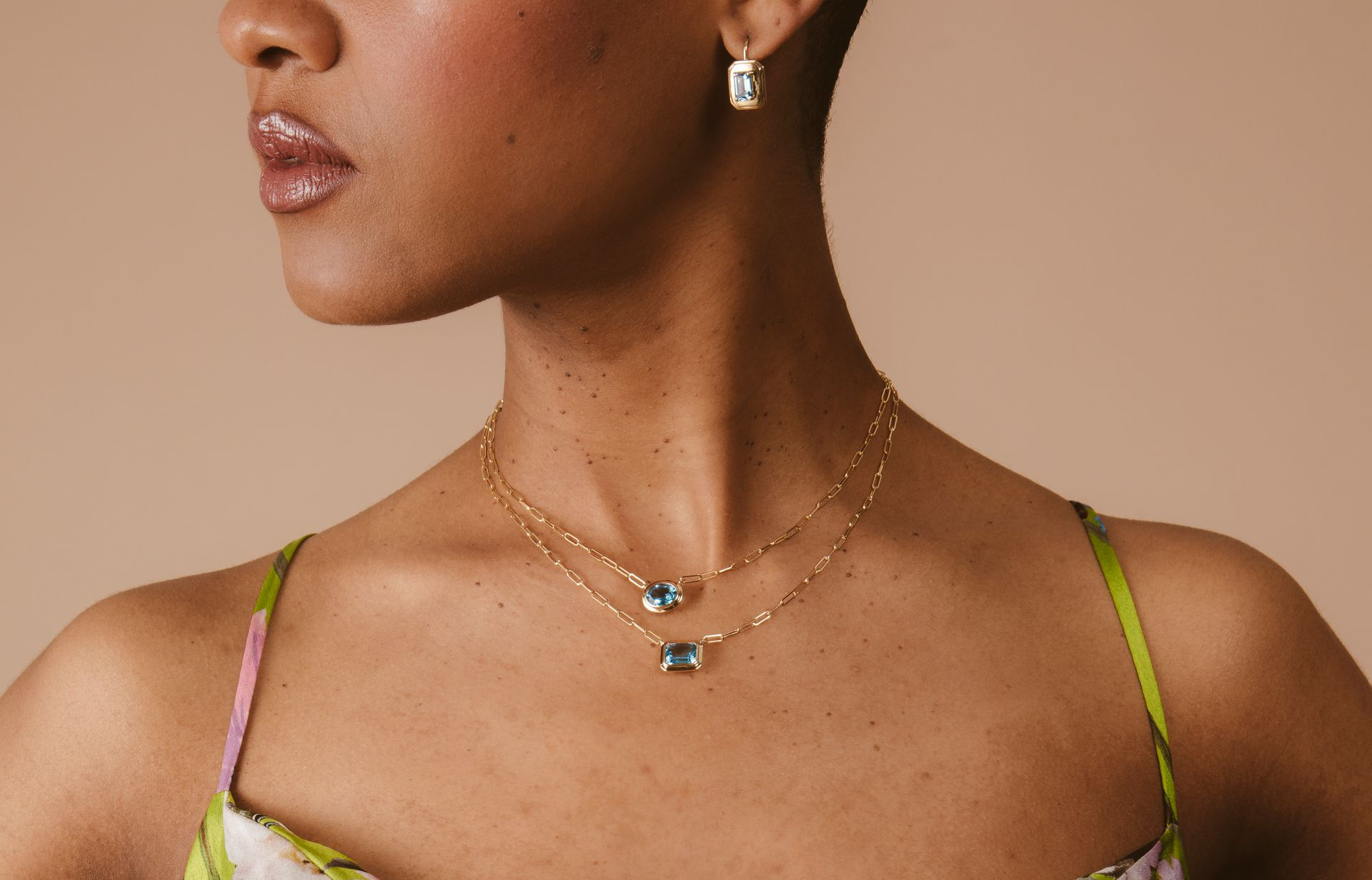 Woman wearing gold necklaces and earrings with rectangular blue gemstones.