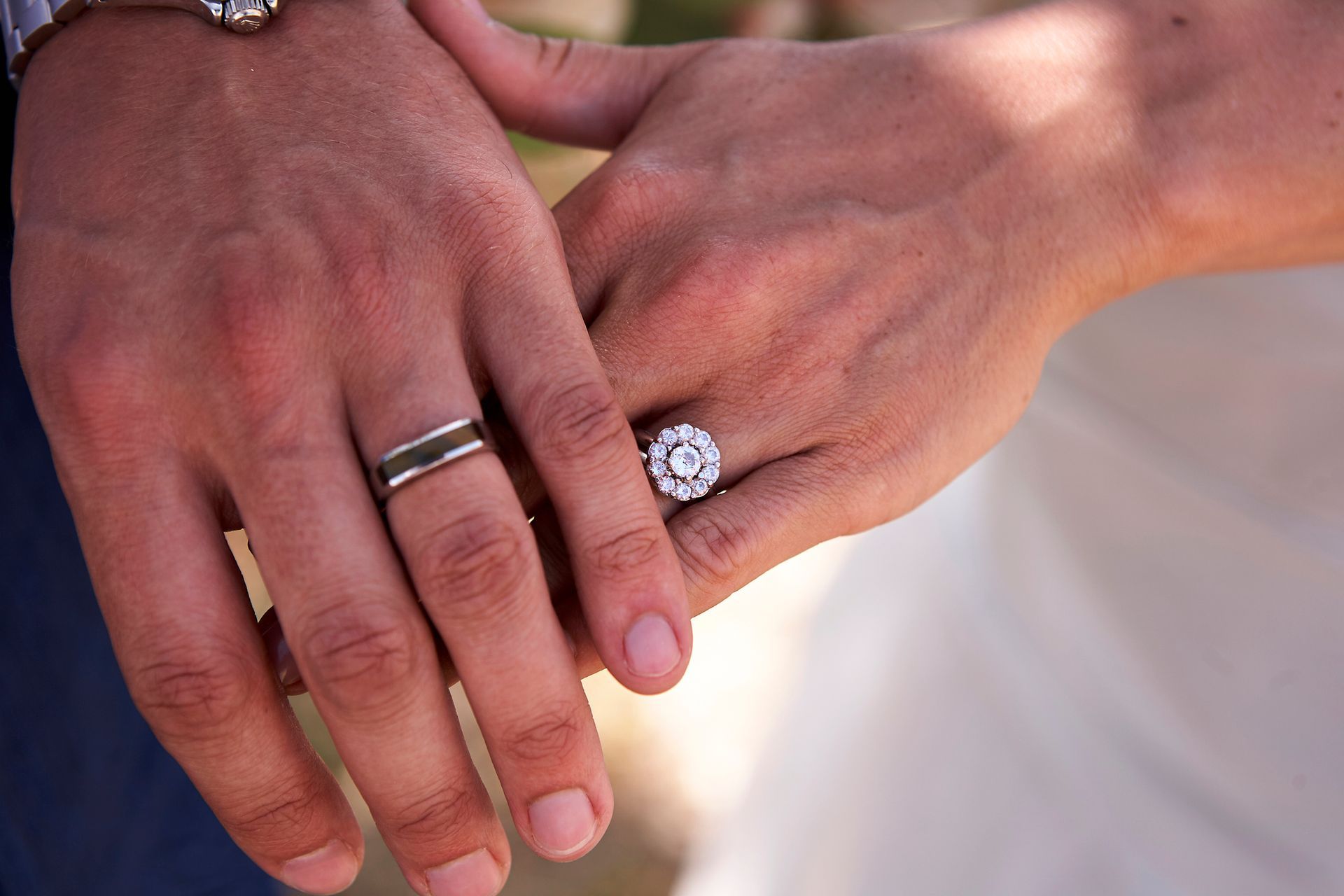 Close-up of two hands, wedding rings visible. One hand has an elaborate engagement ring.