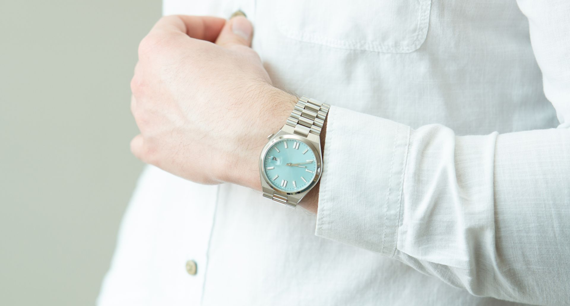 Person wearing a wristwatch with a light blue face and silver band, white shirt sleeve pulled up.