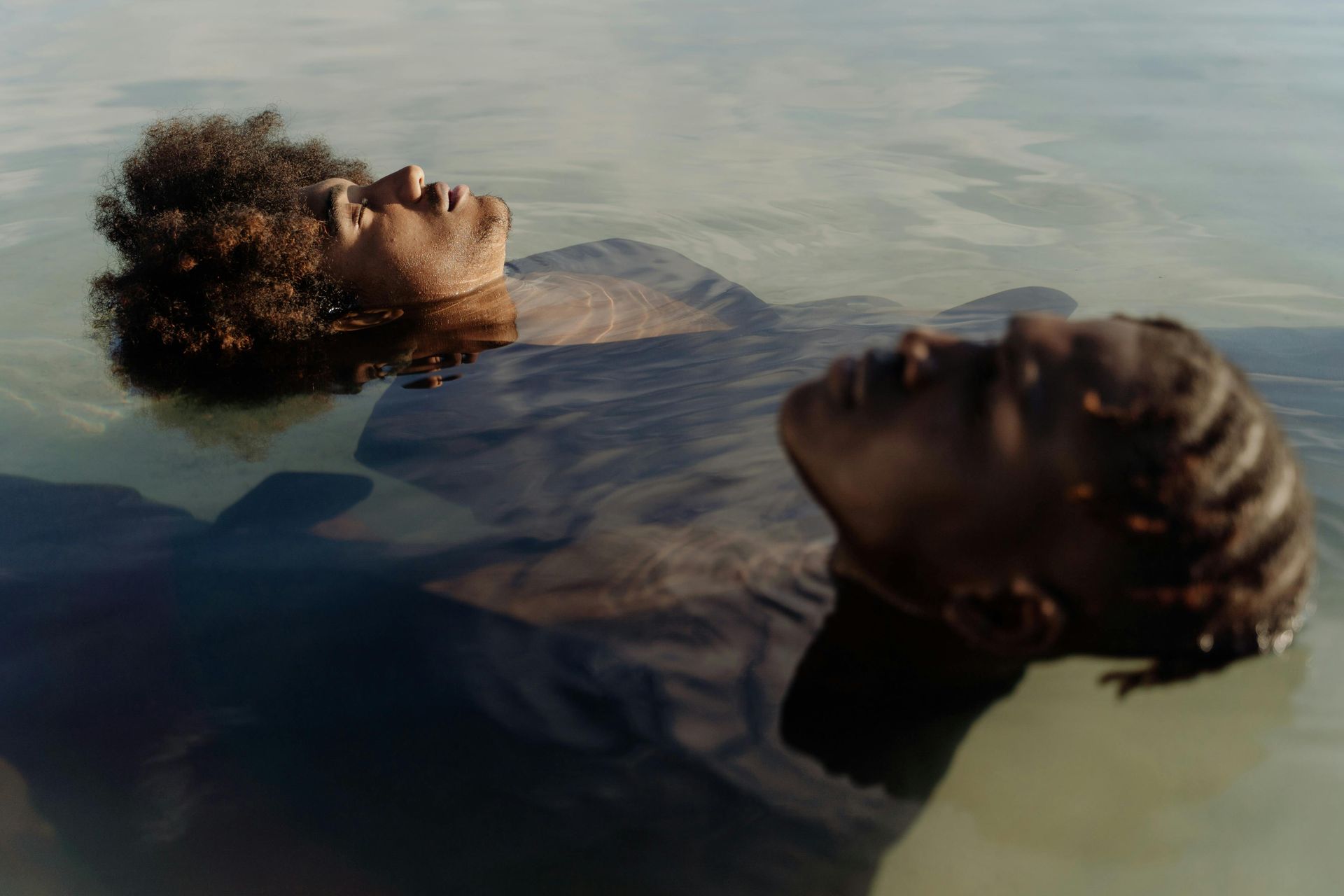 Two individuals floating serenely on their backs in calm water, eyes closed in relaxation.