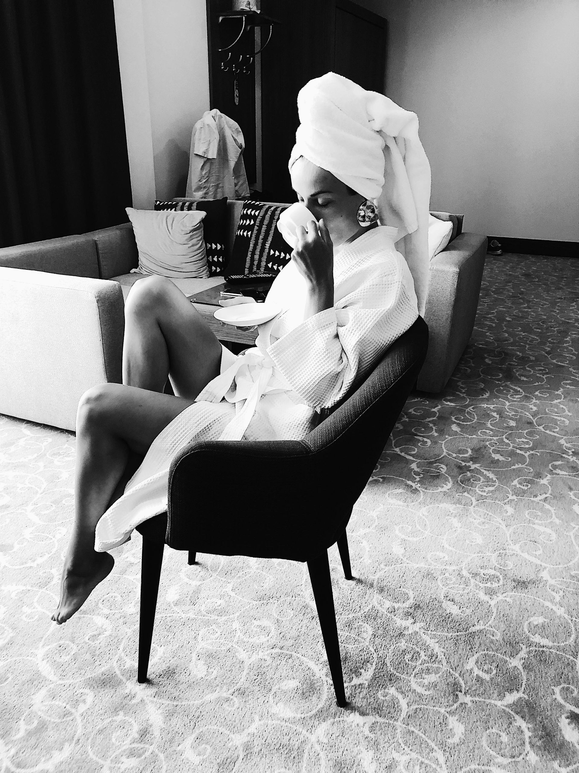 A woman in a robe with a towel wrapped around her head enjoys a cup of tea, embodying relaxation and mindful self-care in a cozy setting.