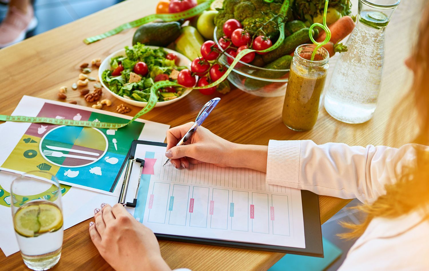 Woman writing on clipboard with healthy food and drinks on table.