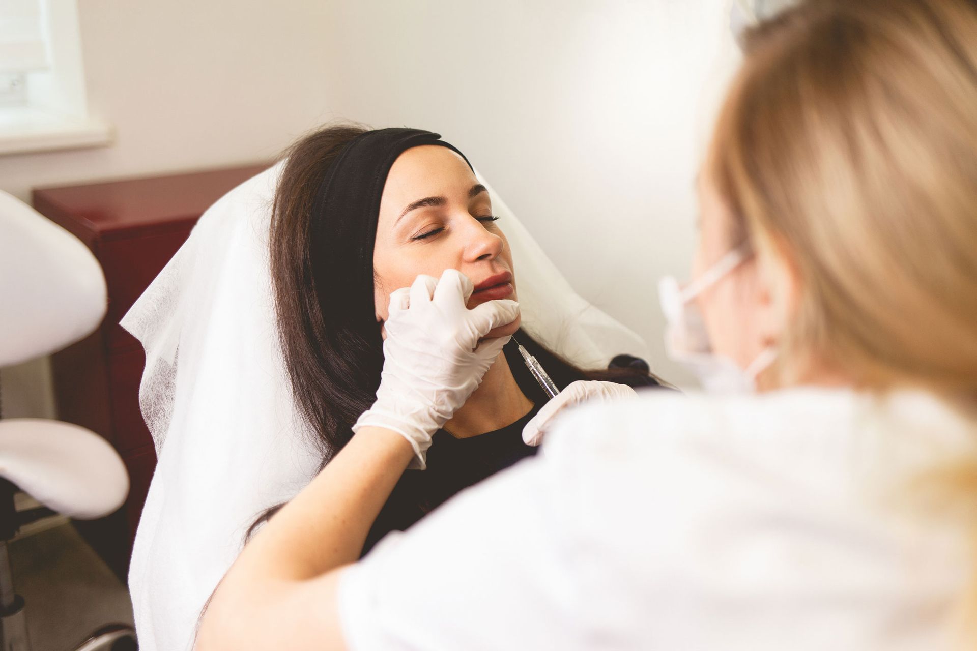 Person receiving lip injections from a person wearing gloves and a mask in a medical setting.