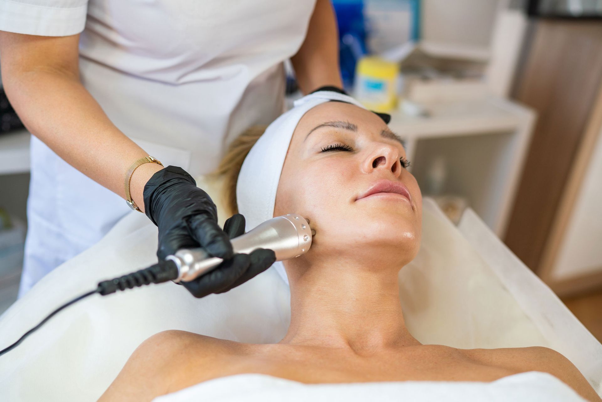 Woman receiving facial treatment with a handheld device. Therapist in black gloves in a spa setting. Woman receiving facial treatment with a handheld device. Therapist in black gloves in a spa setting.