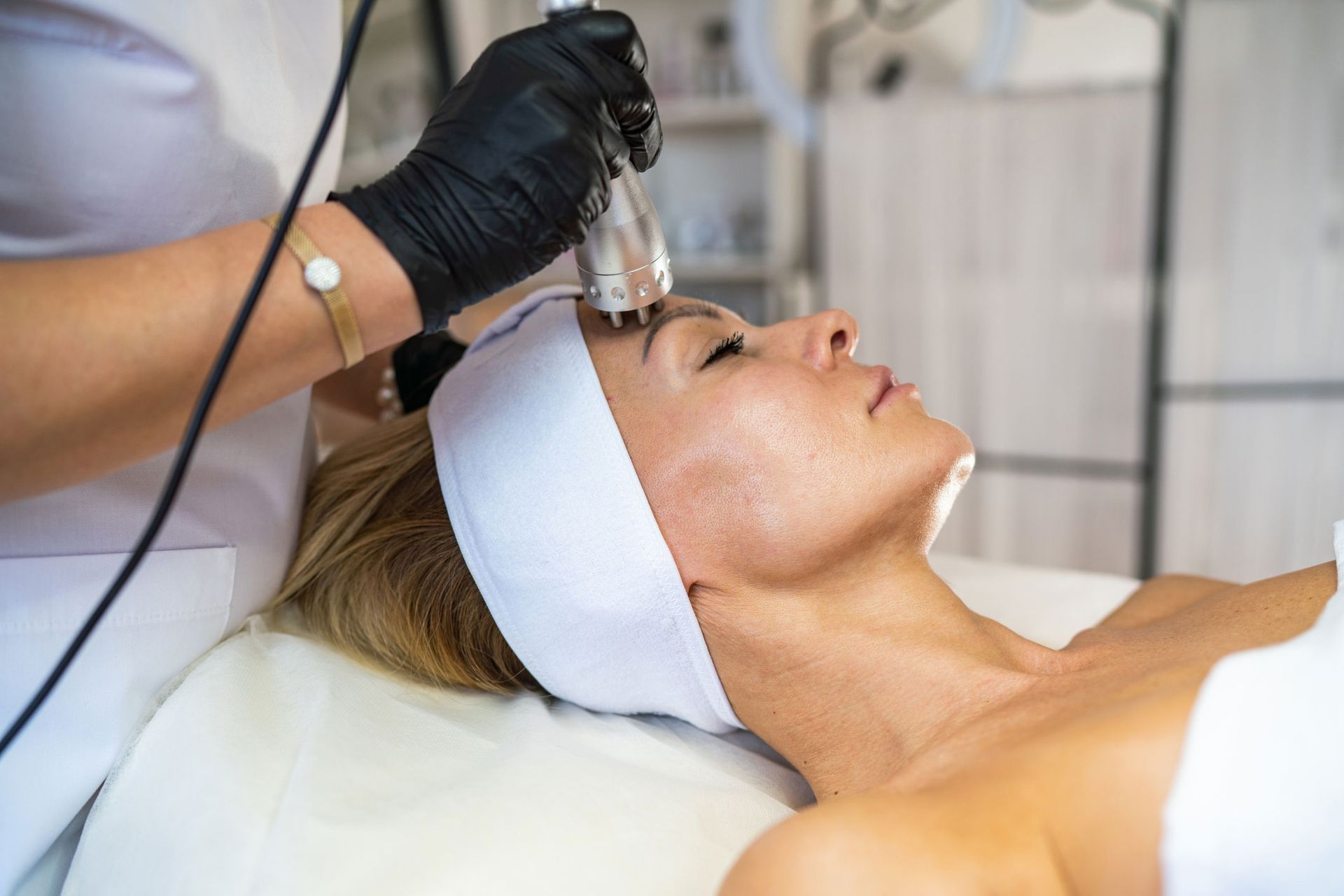 Woman receiving facial treatment in a spa, using a handheld device on her forehead. Woman receiving facial treatment in a spa, using a handheld device on her forehead.
